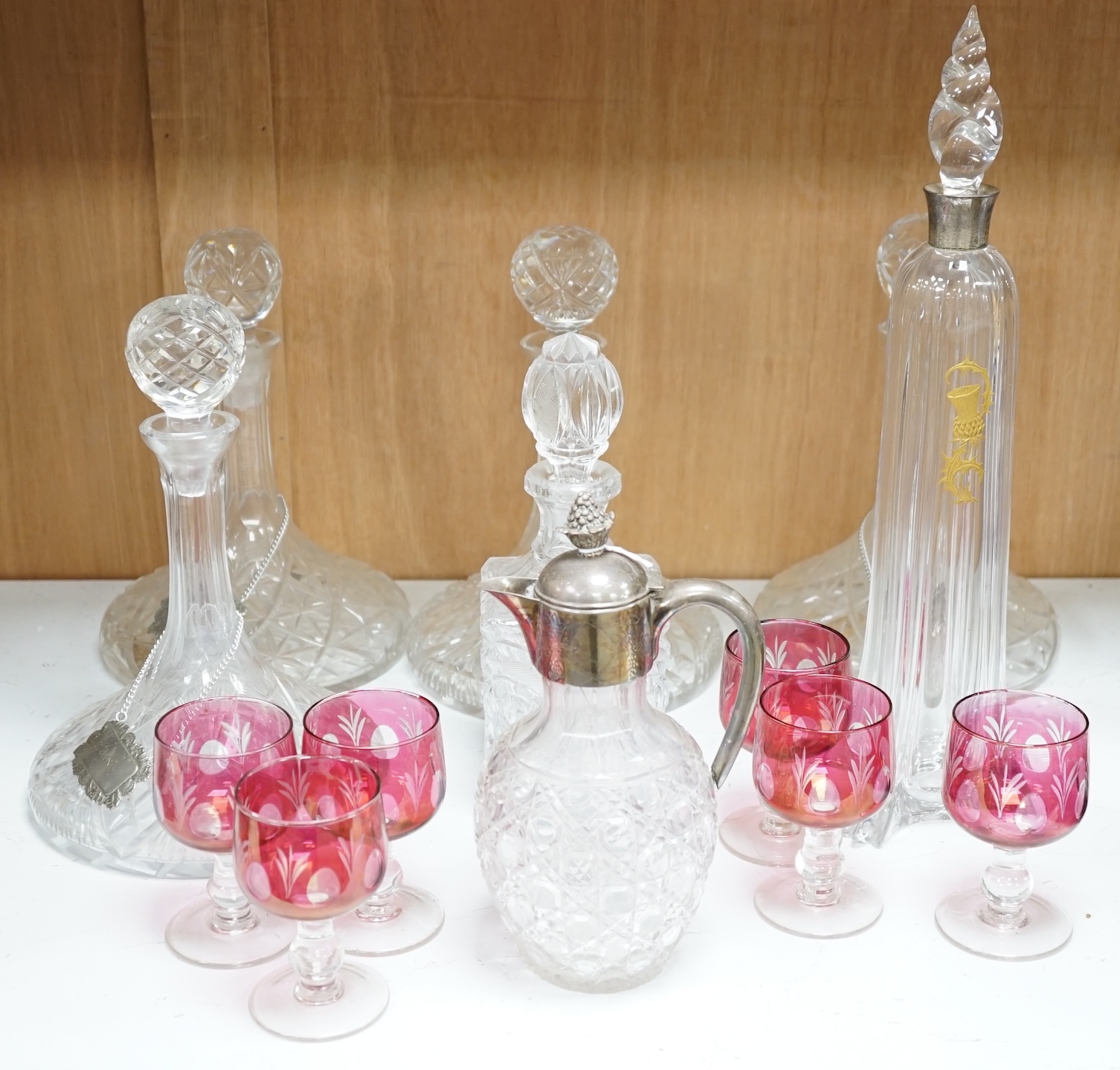 Two pairs of cut glass ships decanters, a square decanter, a ewer and a tall Scottish decanter and six cranberry glasses, tallest 43cm high